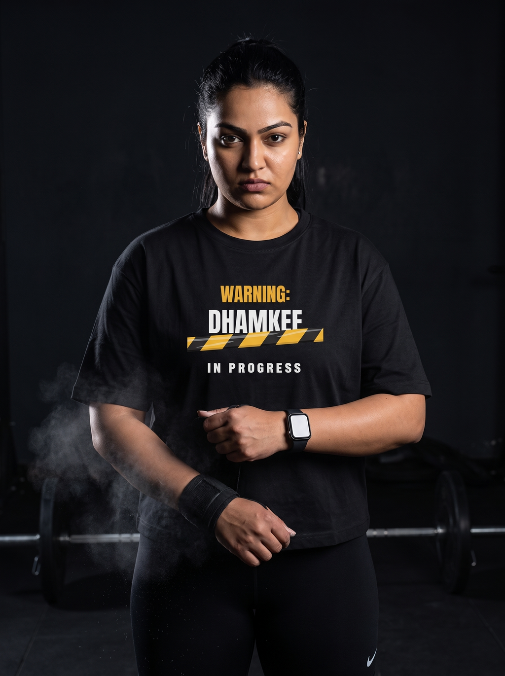 Dhamkee In Progress box fit gym t shirt for women in Black, worn by a model wrapping wrist wraps with chalk dust in the air